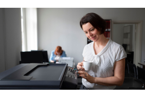 woman standing near printer holding la cup of coffee