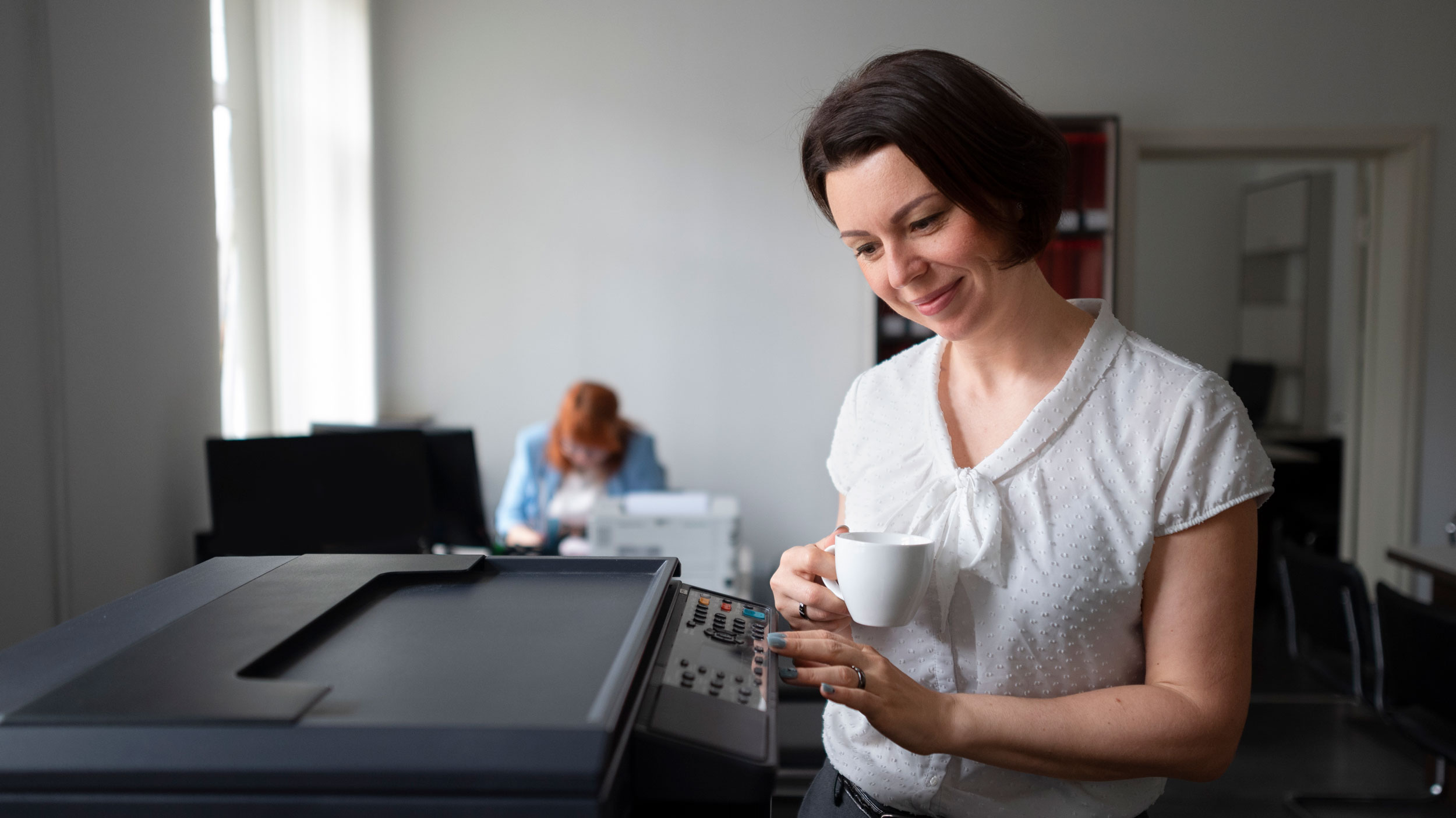 woman standing near printer holding la cup of coffee